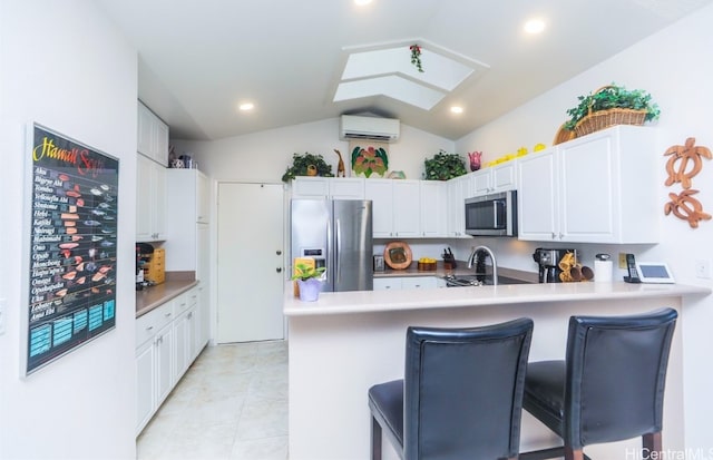 kitchen featuring an AC wall unit, vaulted ceiling, a kitchen bar, white cabinets, and appliances with stainless steel finishes