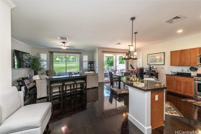 kitchen featuring dark stone counters, ceiling fan with notable chandelier, hanging light fixtures, appliances with stainless steel finishes, and a kitchen island