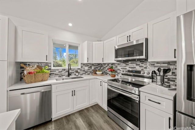 kitchen with appliances with stainless steel finishes, vaulted ceiling, white cabinetry, and sink