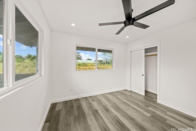 unfurnished bedroom with a closet, multiple windows, ceiling fan, and hardwood / wood-style floors