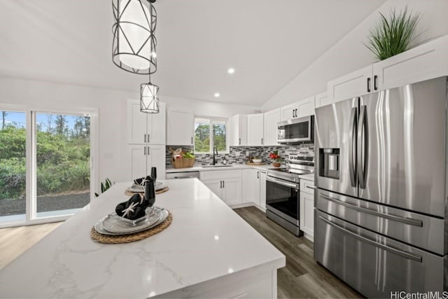 kitchen featuring pendant lighting, lofted ceiling, white cabinets, light stone counters, and stainless steel appliances