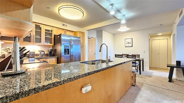 kitchen with sink, stainless steel fridge, dark stone counters, track lighting, and light carpet