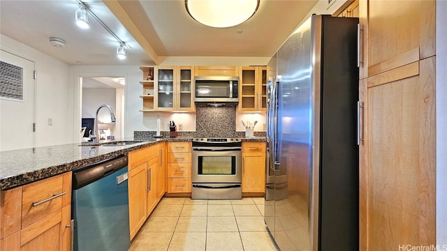 kitchen with appliances with stainless steel finishes, tasteful backsplash, sink, light tile patterned floors, and dark stone countertops