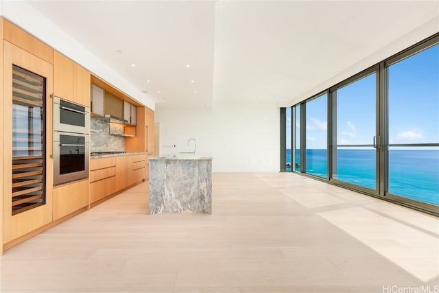 kitchen with backsplash, a water view, light stone countertops, light brown cabinetry, and stainless steel gas cooktop