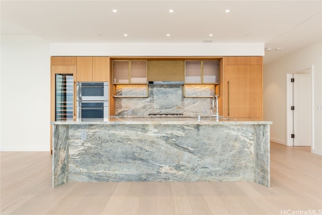 kitchen featuring light stone counters, sink, stainless steel double oven, and light hardwood / wood-style floors