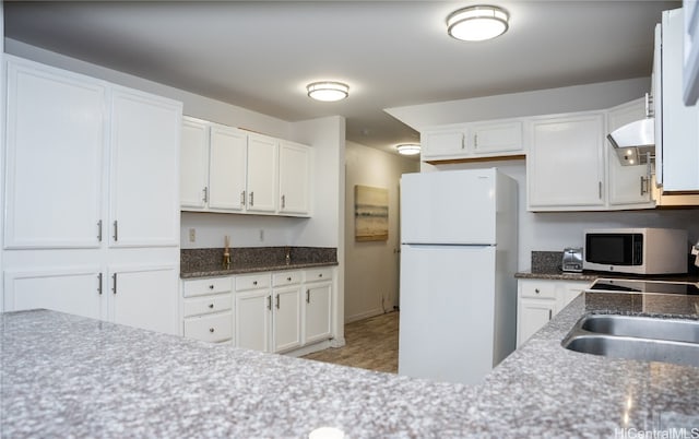 kitchen with white appliances, white cabinetry, dark stone counters, and sink