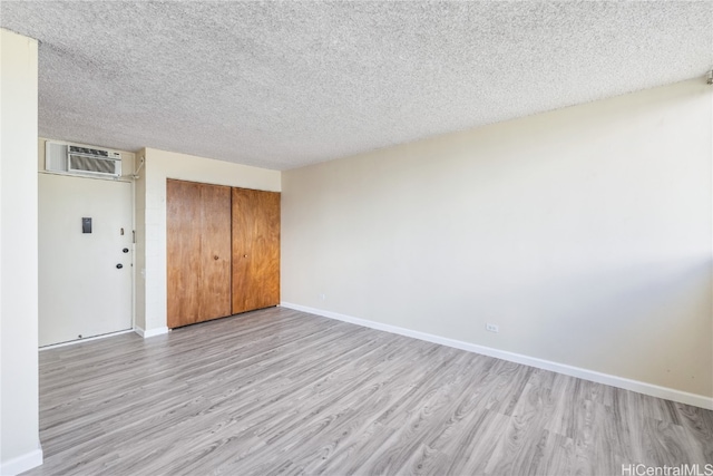 unfurnished bedroom with light hardwood / wood-style floors, an AC wall unit, a textured ceiling, and a closet