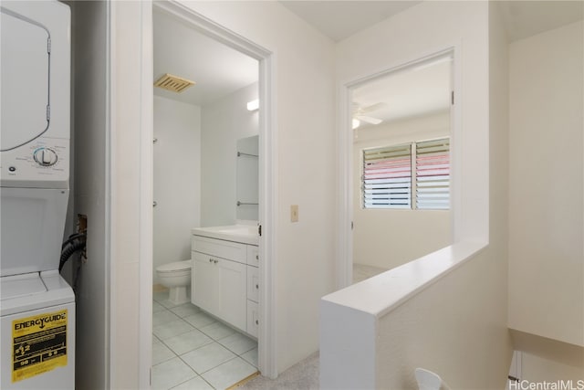 bathroom with stacked washing maching and dryer, tile patterned floors, vanity, ceiling fan, and toilet