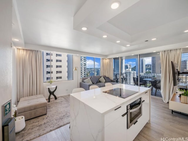 kitchen featuring a raised ceiling, a kitchen island, black electric stovetop, light hardwood / wood-style floors, and white cabinets