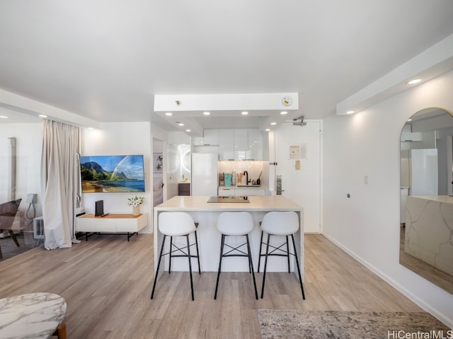 kitchen with backsplash, white cabinets, white refrigerator, light hardwood / wood-style flooring, and a breakfast bar area