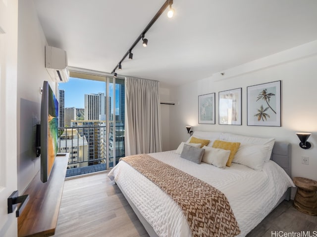 bedroom with rail lighting, a wall mounted air conditioner, expansive windows, light hardwood / wood-style floors, and access to outside