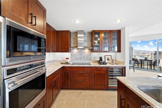 kitchen with light stone countertops, beverage cooler, sink, wall chimney range hood, and oven