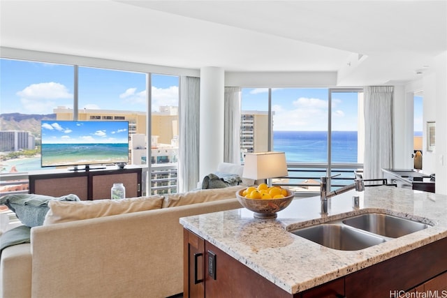 kitchen with a water view, light stone counters, a kitchen island with sink, and sink