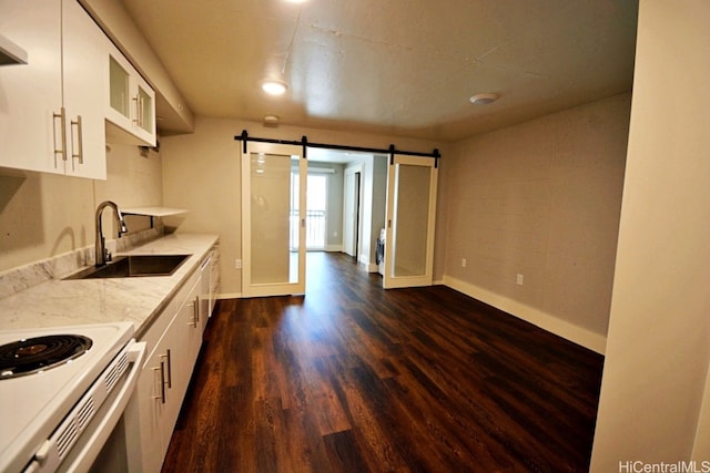 kitchen with light stone countertops, dark hardwood / wood-style flooring, sink, a barn door, and white cabinets