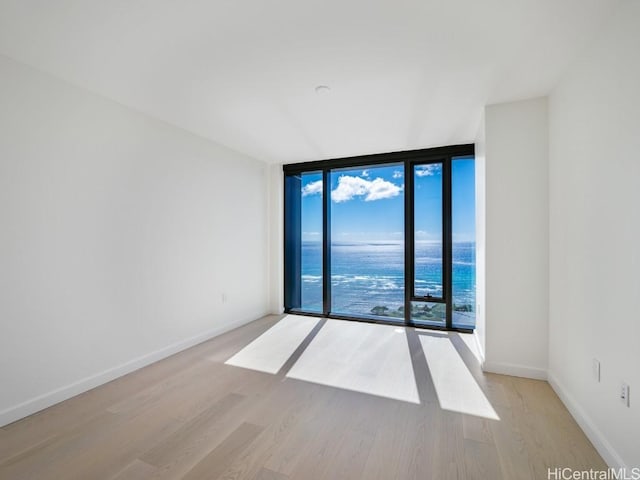 empty room featuring light wood-type flooring, a wall of windows, and a water view