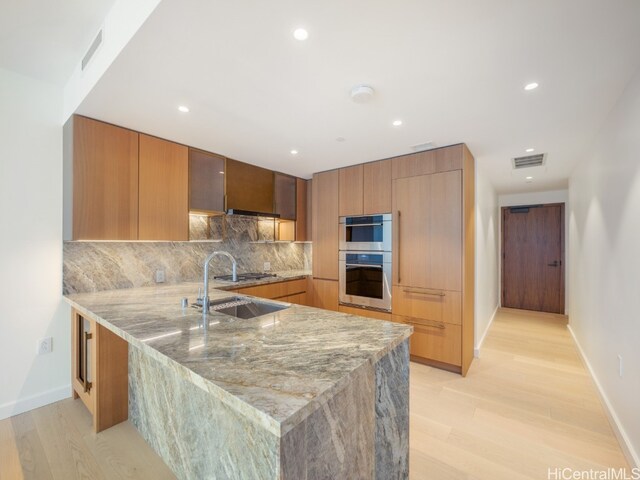 kitchen with backsplash, light stone countertops, light wood-type flooring, appliances with stainless steel finishes, and kitchen peninsula