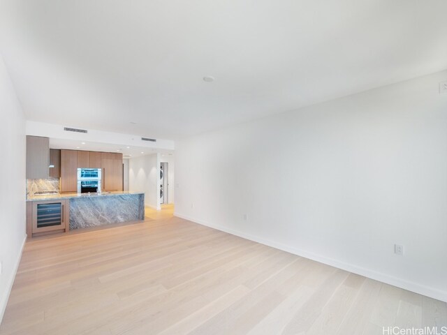 unfurnished living room with wine cooler and light hardwood / wood-style flooring
