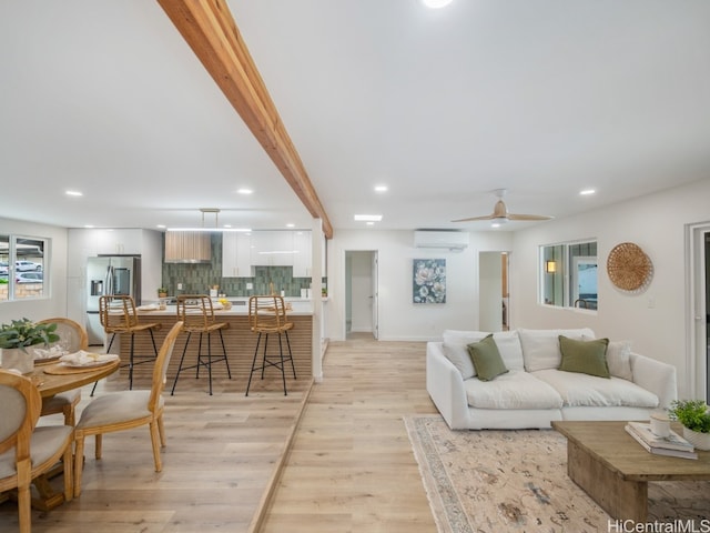 living room featuring ceiling fan, beam ceiling, a wall unit AC, and light hardwood / wood-style flooring