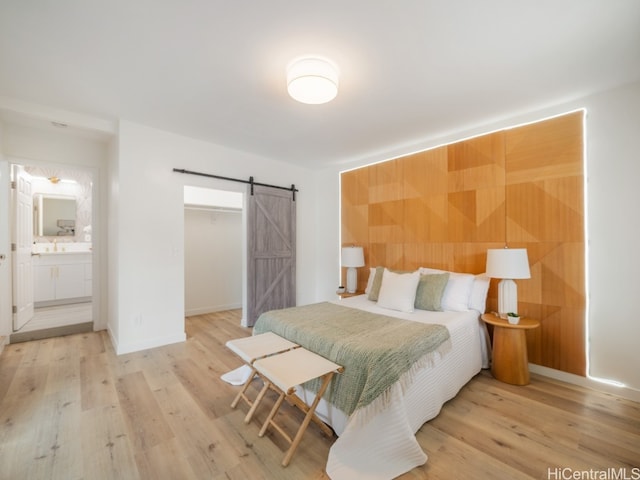 bedroom featuring ensuite bathroom, a barn door, and light hardwood / wood-style flooring