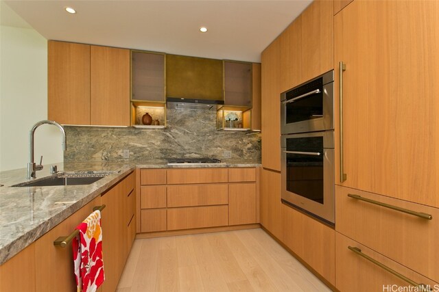 kitchen featuring ventilation hood, sink, light hardwood / wood-style flooring, decorative backsplash, and light stone counters