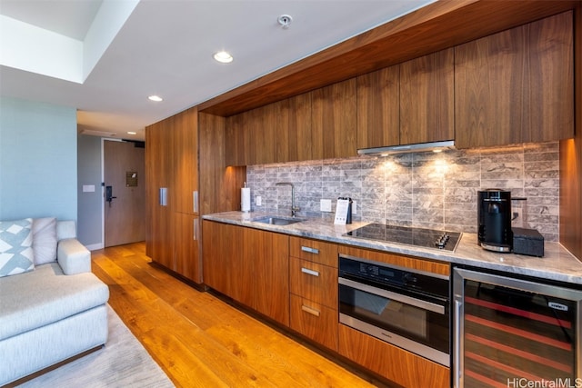 kitchen featuring oven, light hardwood / wood-style flooring, black electric cooktop, tasteful backsplash, and beverage cooler