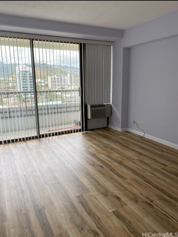 spare room featuring hardwood / wood-style flooring, an AC wall unit, and a textured ceiling