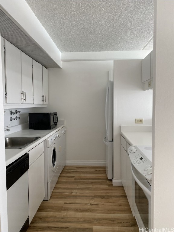 kitchen with sink, hardwood / wood-style floors, white appliances, washer / dryer, and white cabinets