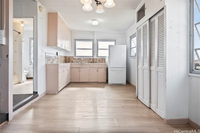 kitchen featuring sink, tasteful backsplash, ornamental molding, white fridge, and light wood-type flooring