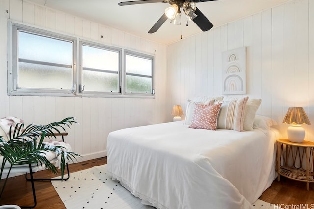 bedroom featuring hardwood / wood-style flooring, ceiling fan, and wood walls