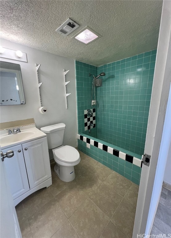 bathroom featuring a tile shower, vanity, a textured ceiling, tile patterned flooring, and toilet