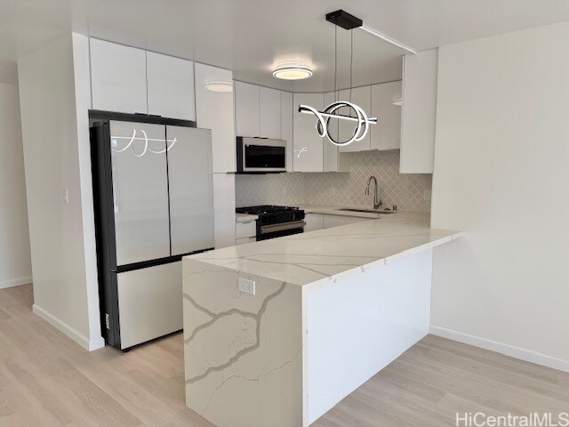 kitchen featuring white cabinetry, sink, stainless steel appliances, hanging light fixtures, and light wood-type flooring