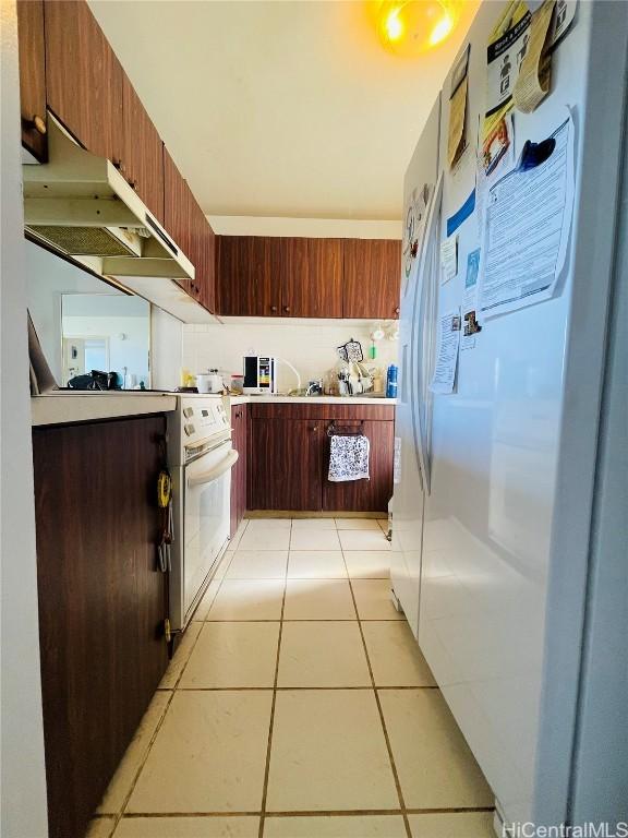 kitchen with white refrigerator, range hood, and light tile patterned flooring