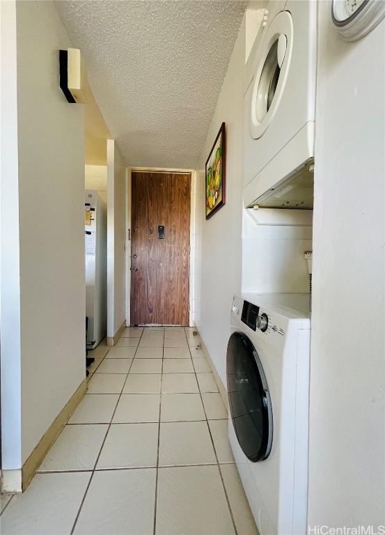 laundry area featuring light tile patterned flooring, a textured ceiling, and stacked washer and clothes dryer