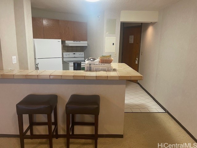 kitchen with tile counters, kitchen peninsula, white appliances, a kitchen bar, and light carpet