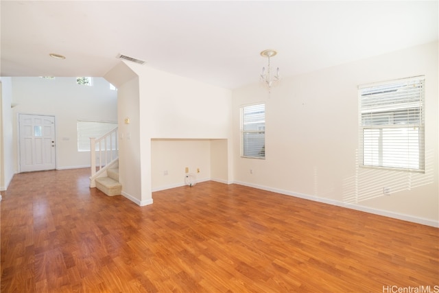 unfurnished living room featuring plenty of natural light, an inviting chandelier, wood-type flooring, and vaulted ceiling