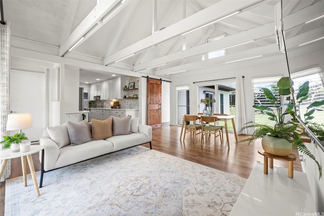 living room with high vaulted ceiling, a barn door, beamed ceiling, and wood finished floors