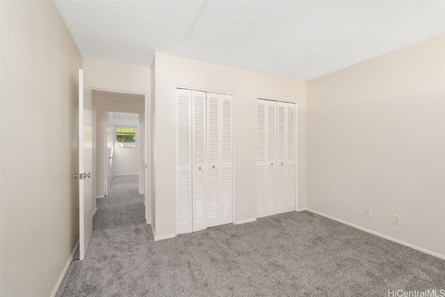 unfurnished bedroom featuring a textured ceiling, light carpet, and multiple closets