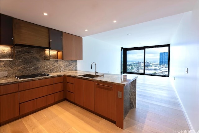 kitchen featuring floor to ceiling windows, sink, stainless steel gas cooktop, kitchen peninsula, and light hardwood / wood-style floors