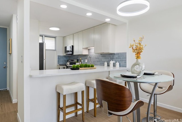 kitchen with appliances with stainless steel finishes, tasteful backsplash, sink, light hardwood / wood-style flooring, and white cabinetry