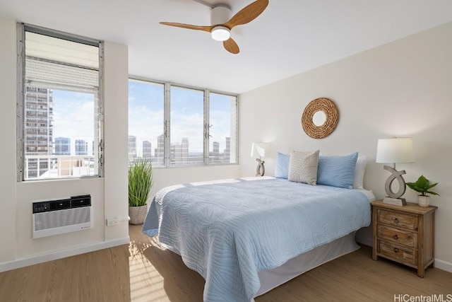 bedroom featuring a wall mounted air conditioner, wood-type flooring, and ceiling fan