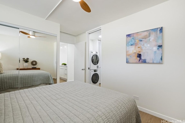 bedroom featuring wood-type flooring, stacked washer / dryer, and ceiling fan