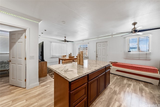 kitchen with light stone countertops, a center island, light hardwood / wood-style floors, and ceiling fan