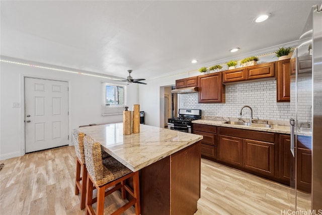 kitchen featuring sink, ornamental molding, light hardwood / wood-style floors, light stone counters, and gas stove