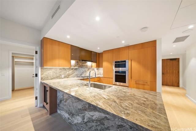 kitchen featuring sink, light hardwood / wood-style flooring, light stone countertops, kitchen peninsula, and stainless steel double oven