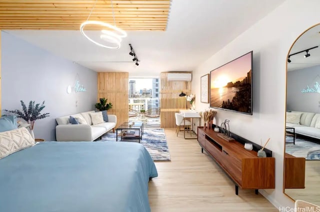 bedroom with a wall mounted AC, light hardwood / wood-style floors, and track lighting