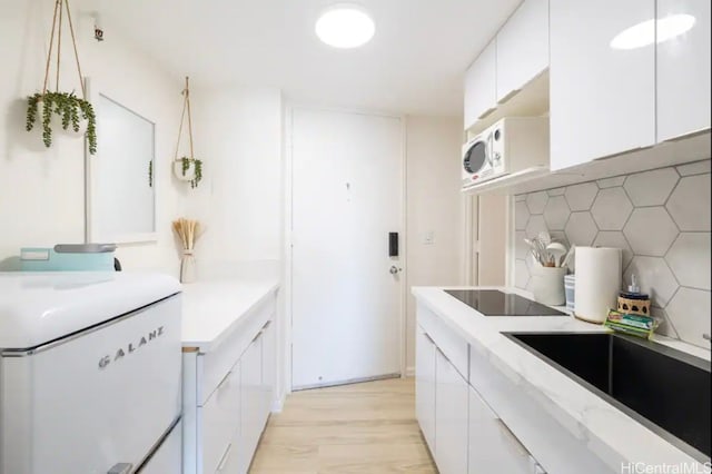 kitchen with tasteful backsplash, white appliances, sink, white cabinets, and light hardwood / wood-style floors