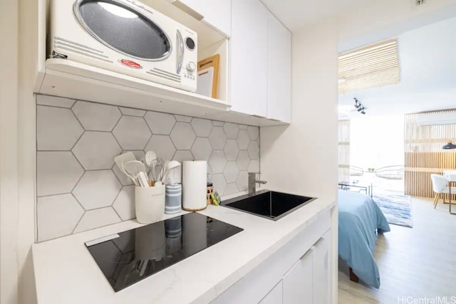 kitchen featuring white cabinets, black electric stovetop, backsplash, and sink