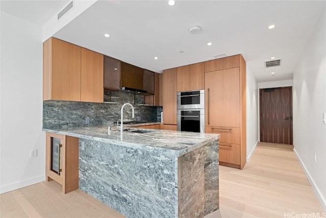 kitchen featuring tasteful backsplash, modern cabinets, a peninsula, light stone countertops, and double oven