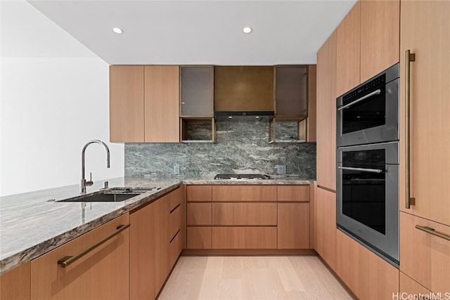 kitchen featuring decorative backsplash, appliances with stainless steel finishes, light stone counters, light wood-style floors, and a sink