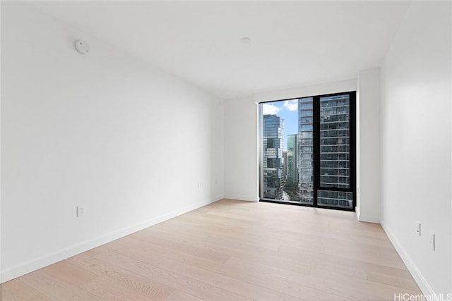 unfurnished room featuring baseboards, light wood-type flooring, and a city view